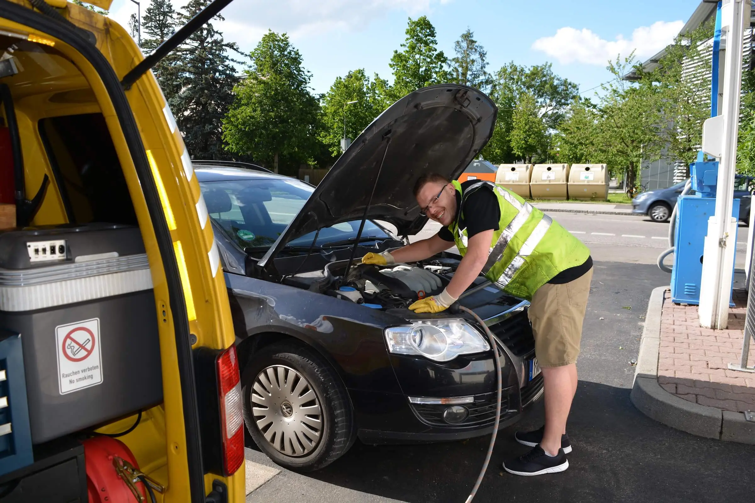 FTH-Techniker beugt sich über den Motorraum eines VW Passat, daneben der gelbe Einsatzwagen mit Abpumpschlauch