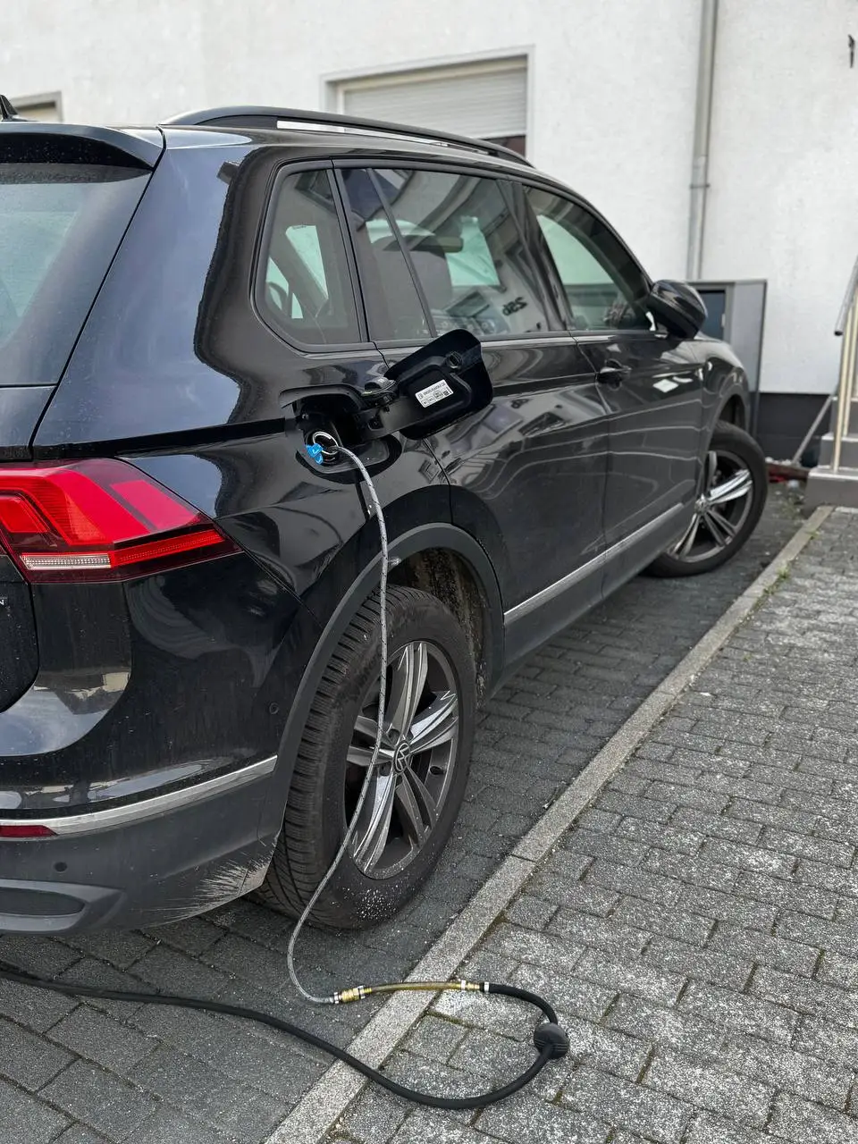 Schwarzer SUV auf einem Hof, ein Schlauch führt vom Tankstutzen zum Boden